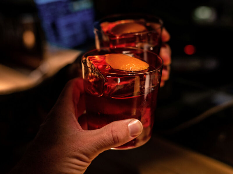 Zwei Gläser Negroni stoßen in einer eleganten Bar in Brera, Mailand, an – Symbol für Geselligkeit, italienische Aperitivo-Kultur und die zeitlose Faszination dieses ikonischen Cocktails.