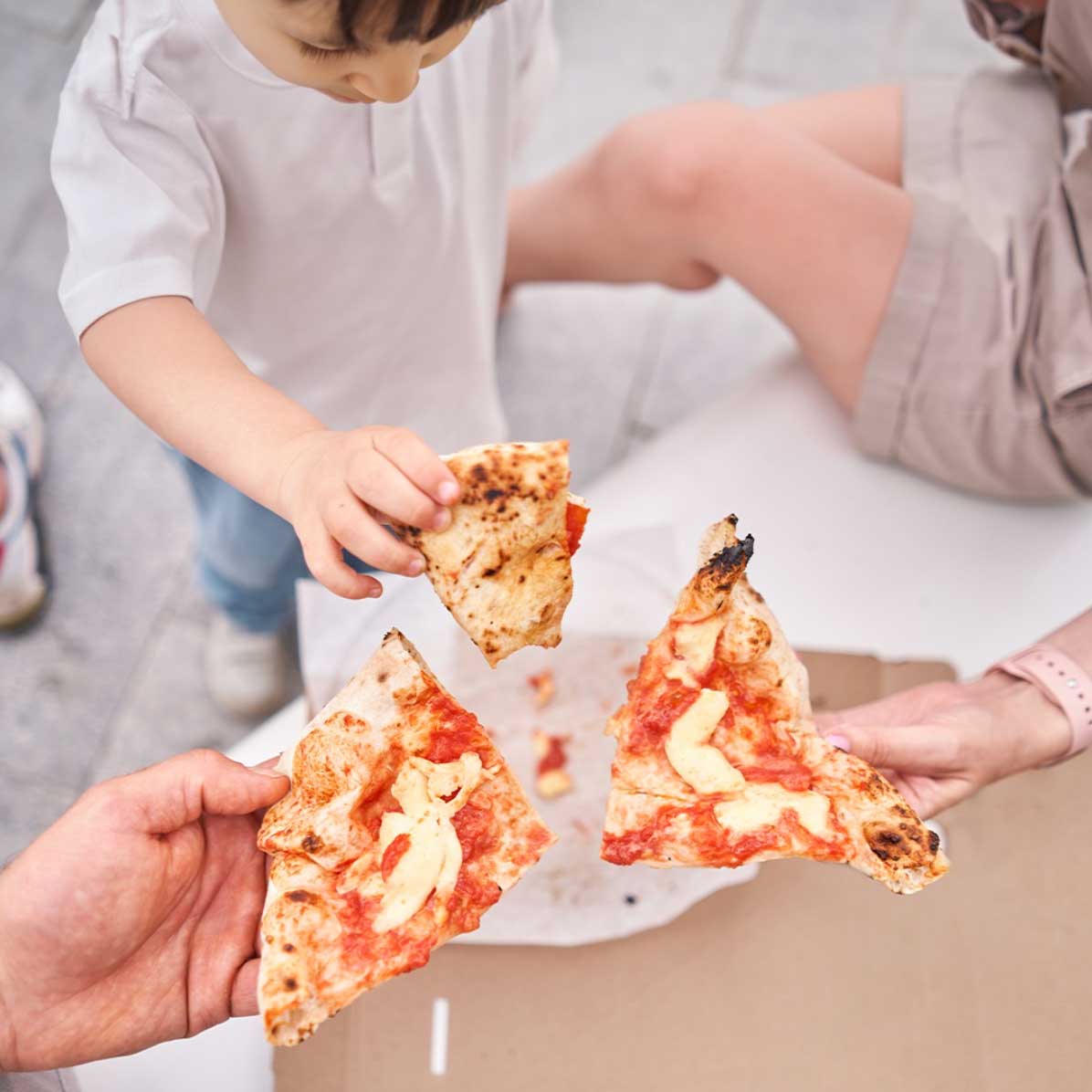 Ein Kind greift nach einem Stück Pizza, das mit Caputo-Mehl hergestellt wurde. Im Hintergrund teilen weitere Hände Pizzastücke, die auf der Caputo-Mehlbasis gebacken wurden