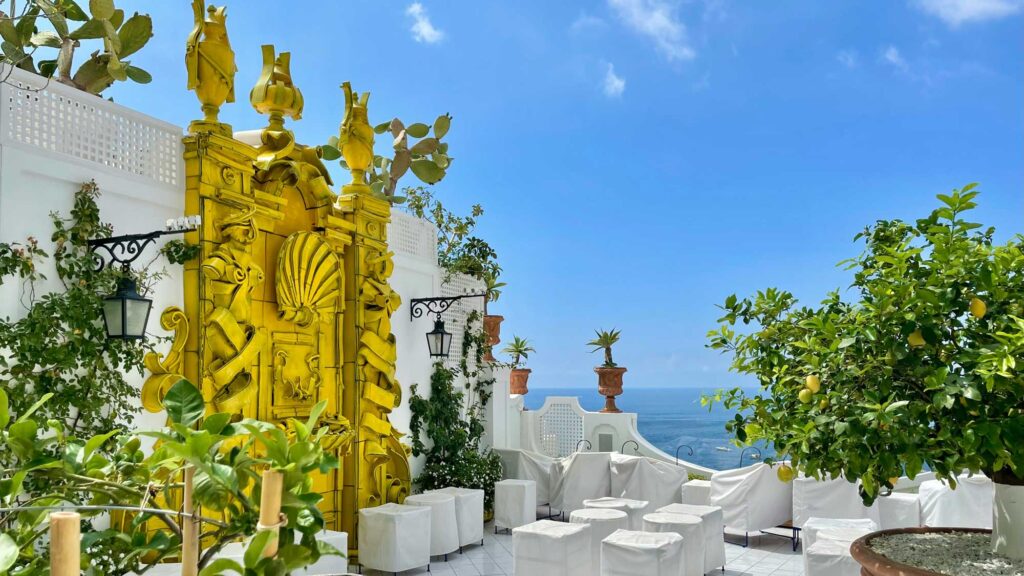 Eine malerische Terrasse an der italienischen Küste, geschmückt mit Zitronenbäumen und einem dekorativen gelben Tor, mit Blick auf das Mittelmeer. Diese Szene spiegelt die typische Umgebung wider, in der die Zitronen für die Limoncello-Herstellung wachsen