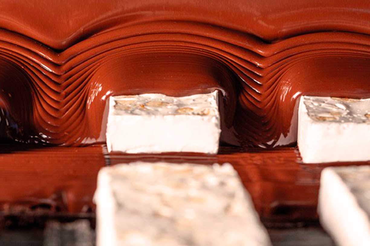 Frische Nougatriegel, die mit einer Schicht aus reichhaltiger, geschmolzener Schokolade überzogen werden und eine der köstlichen Produktionsphasen bei Antica Torroneria Piemontese veranschaulichen