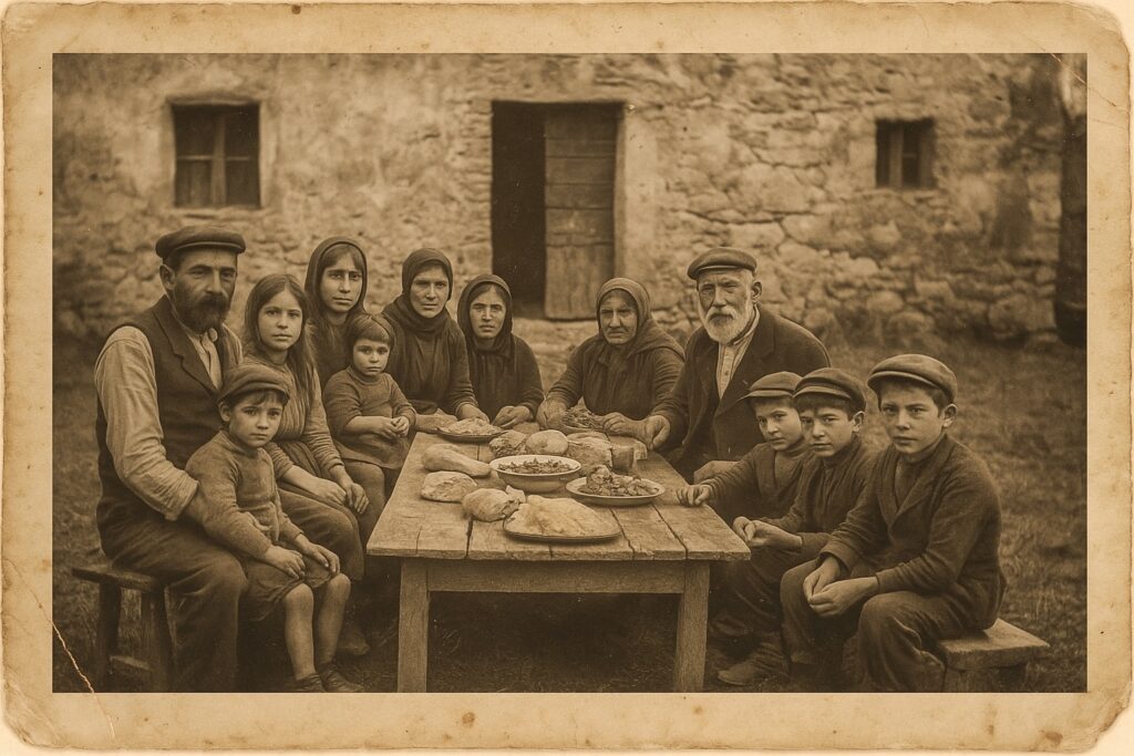 Historische Fotografie einer italienischen Bauernfamilie der 1920er Jahre: mehrere Generationen sitzen vor einem alten Bauernhaus an einem Holztisch im Freien, gedeckt mit einfachem Essen, in Sepia mit sichtbaren Alterungsspuren.
