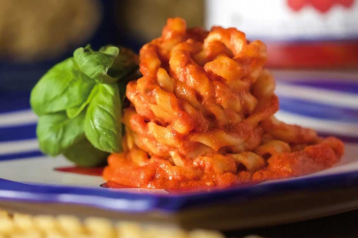 Frische Pasta von Pastificio Gentile, angerichtet mit einer aromatischen Tomatensauce und garniert mit einem Basilikumblatt. Ein Gericht, das für die Qualität und den unverwechselbaren Geschmack der Pasta aus Gragnano steht