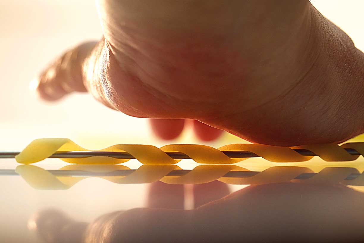 Detaillierte Aufnahme einer Hand, die ein spiralförmiges Nudelstück auf einer Arbeitsfläche rollt. Darstellung des handwerklichen Ansatzes und der Hingabe zur Qualität bei Pastificio Gentile