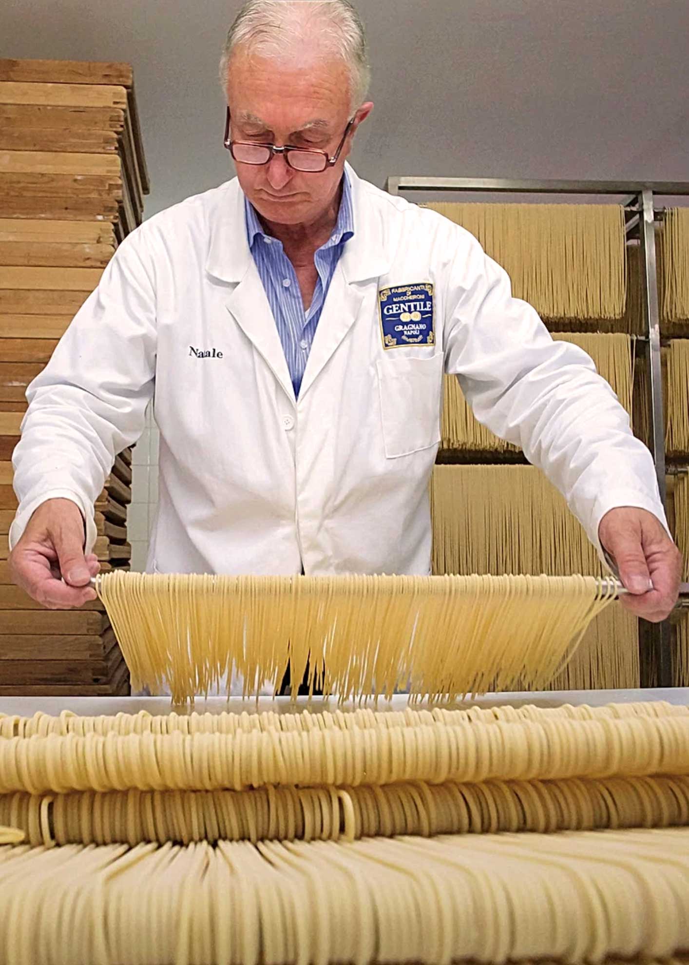 Ein Mitarbeiter von Pastificio Gentile in einem weißen Kittel, der die hängende Pasta während des Trocknungsprozesses kontrolliert. Die Szene unterstreicht die Sorgfalt und das traditionelle Handwerk in der Pastaherstellung bei Pastificio Gentile in Gragnano, Italien