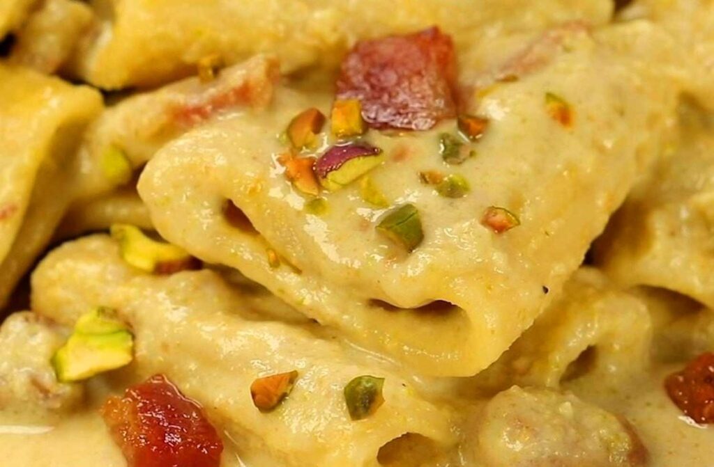 Nahaufnahme von cremigen Paccheri-Nudeln, überzogen mit einer reichhaltigen Pistaziensauce, garniert mit knusprigen Pancetta-Stücken und einem Hauch von zerstoßenen Pistazien, ein klassisches italienisches Gericht.