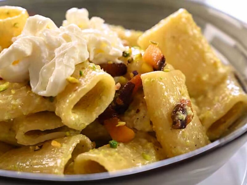 Paccheri-Nudeln, belegt mit Burrata, knusprigem Pancetta und Pistazien, serviert in einer Schüssel mit einer glatten und cremigen Pistaziensauce, perfekt für einen Artikel über ein herzhaftes italienisches Rezept.