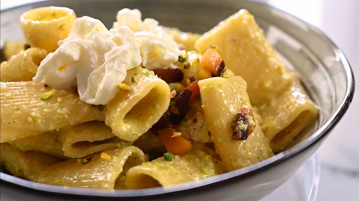 Paccheri-Nudeln, belegt mit Burrata, knusprigem Pancetta und Pistazien, serviert in einer Schüssel mit einer glatten und cremigen Pistaziensauce, perfekt für einen Artikel über ein herzhaftes italienisches Rezept.