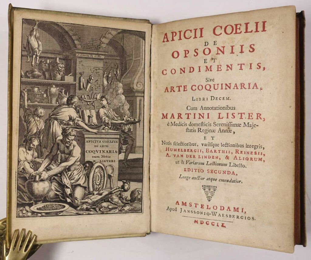 Historische Buchseite aus dem Werk „Apicii Coelii de Opsoniis et Condimentis, sive Arte Coquinaria“ mit einer kunstvollen Illustration und lateinischem Text. Links ist eine detaillierte Gravur zu sehen, die eine antike Küchenszene zeigt: mehrere Figuren bereiten Mahlzeiten zu, umgeben von Küchenutensilien und hängendem Fleisch. Auf der rechten Seite ist der Titel des Buches in roten und schwarzen Buchstaben abgedruckt. Das Werk, welches dem antiken römischen Gourmet Apicius zugeschrieben wird, enthält Rezepte und Anweisungen zur Kochkunst. Diese Darstellung wird in einem Centro Italia Gazzetta Blogbeitrag über die Geschichte und kulturelle Bedeutung der Pasta in Italien verwendet, um die antiken Ursprünge und die Entwicklung der kulinarischen Tradition zu illustrieren