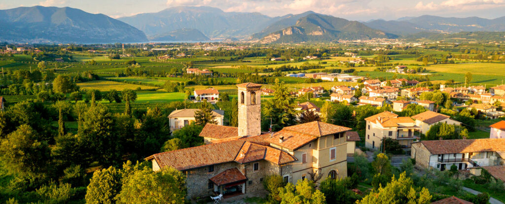 Ein malerisches Dorf in Franciacorta, umgeben von Weinbergen und sanften Hügeln, mit einem historischen Glockenturm im Vordergrund. Ein Symbol für die Tradition und Kultur dieser Region.