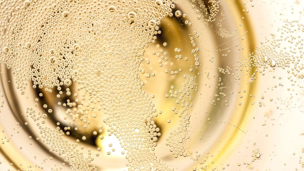 Detailaufnahme von sprudelnden goldenen Bläschen in einem Glas Franciacorta-Schaumwein, die die Eleganz und Qualität des Getränks symbolisieren.