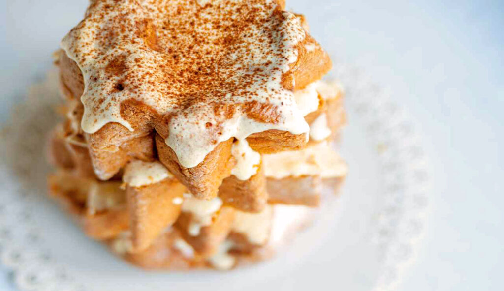 Ein kreativer Turm aus Pandoro-Stücken, geschichtet und verziert mit cremiger Zabaione-Creme, bestreut mit einer Prise Kakao. Ein perfektes Dessert für die Festtage.