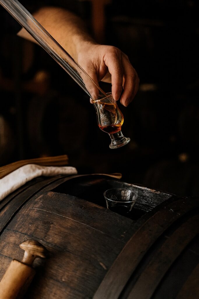 Traditionelle Verkostung: Hand füllt gereiften Balsamico-Essig mit Glaspipette in ein Degustierglas direkt aus dem Holzfass.