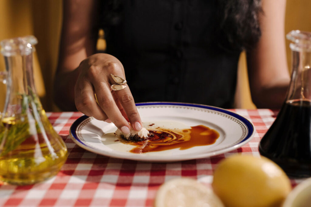 Genussmoment: Frau tunkt frisches Brot in eine Mischung aus Olivenöl und Aceto Balsamico auf italienischer Tischdecke.
