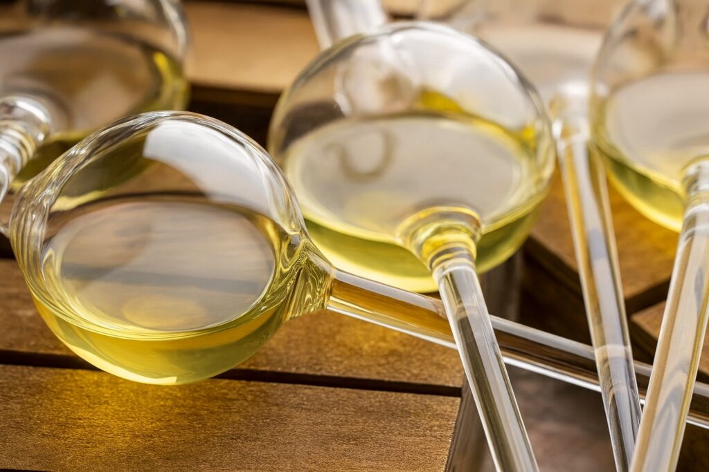 Mehrere Glaspipetten gefüllt mit goldenem Vermentino-Essig, arrangiert auf einem Holztisch – edler Weißweinessig mit intensivem Aroma in der Nahaufnahme.