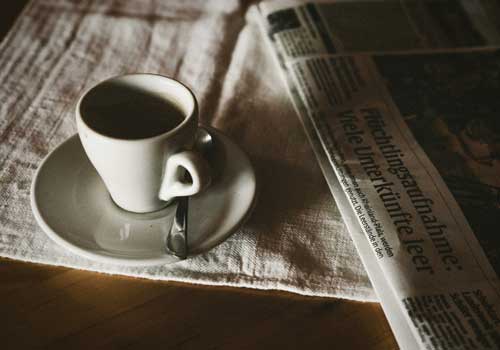 Eine Tasse Espresso auf einem Unterteller mit Löffel, daneben eine aufgeschlagene Zeitung mit sichtbarer Schlagzeile. Stimmungsvolle, nostalgische Atmosphäre – Symbolbild für die Presse- und Nachrichtenrubrik von Centro Italia