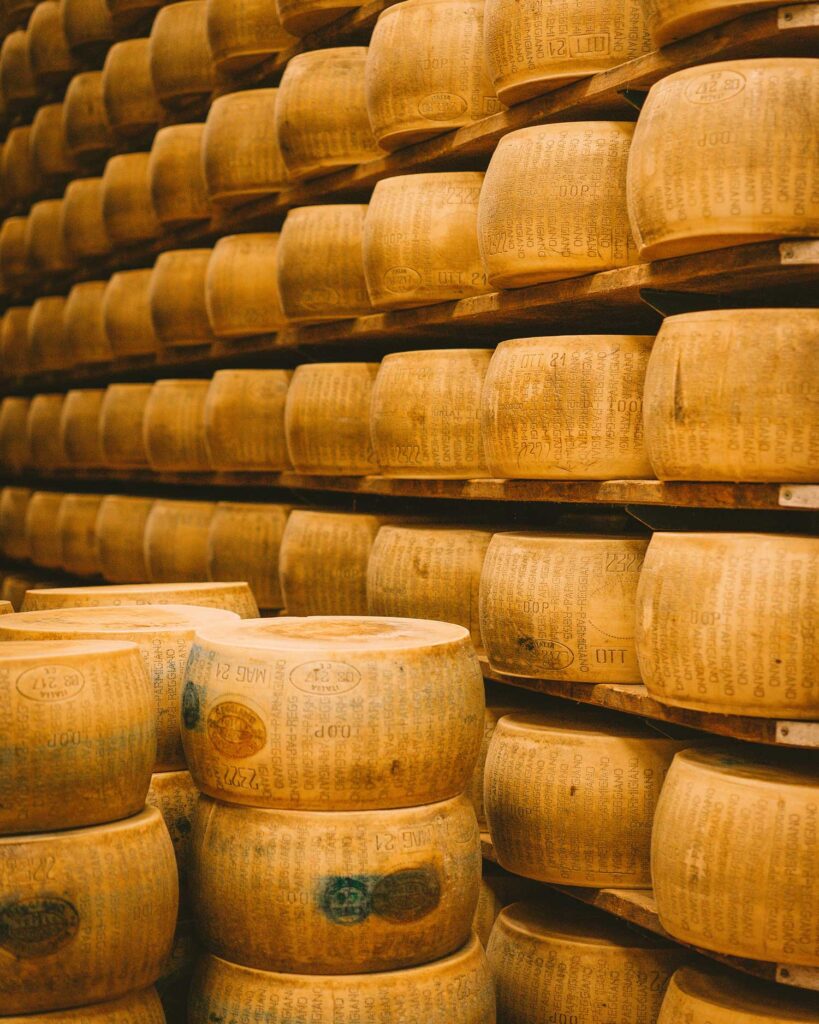 Reihen von gereiften Parmigiano Reggiano Käselaiben in einem traditionellen italienischen Lagerhaus. Die typischen Prägungen auf der Rinde bestätigen die geschützte Ursprungsbezeichnung (g.U.).