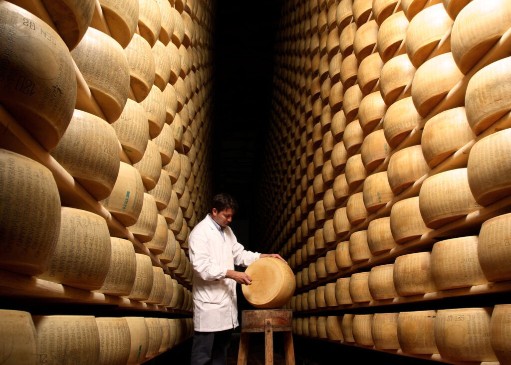 Reifung von Parmigiano Reggiano: Käselaibe lagern in hohen Regalen, während ein Kontrolleur die Qualität des italienischen Hartkäses prüft.