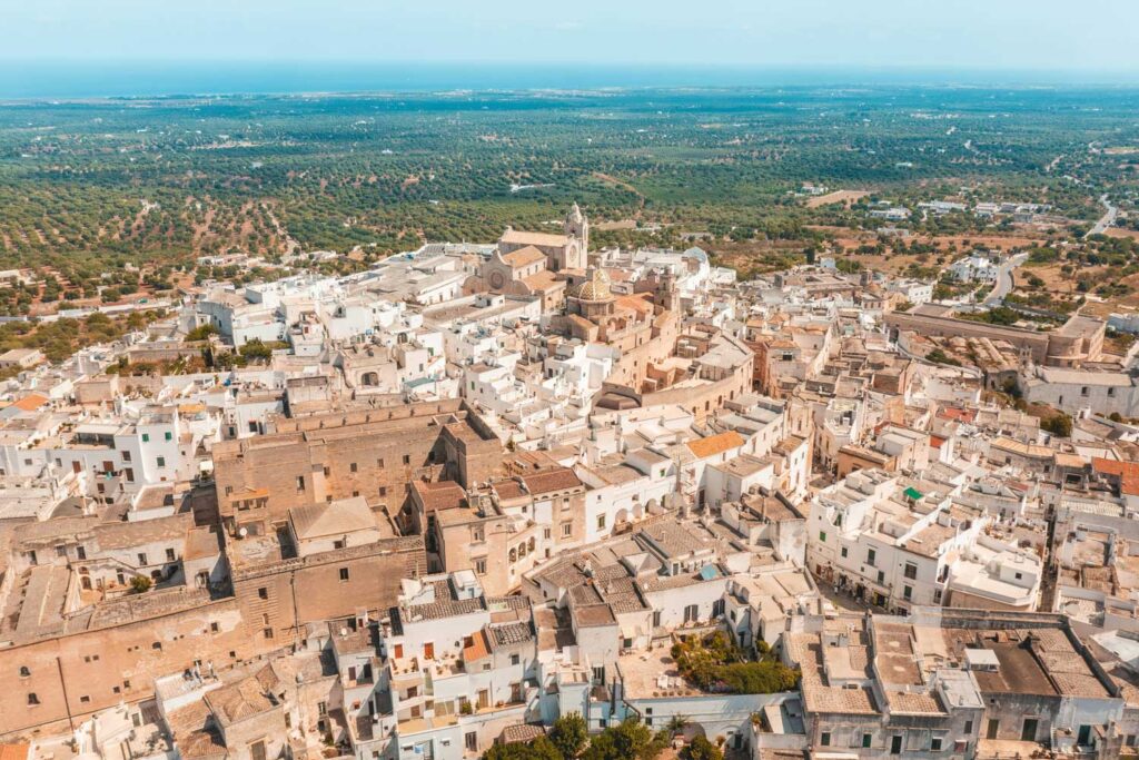 Luftaufnahme der Stadt Ostuni in Apulien, bekannt als die “weiße Stadt”. Die hellen Häuser erstrecken sich über die Hügel mit einem atemberaubenden Blick auf das Umland und das Meer.