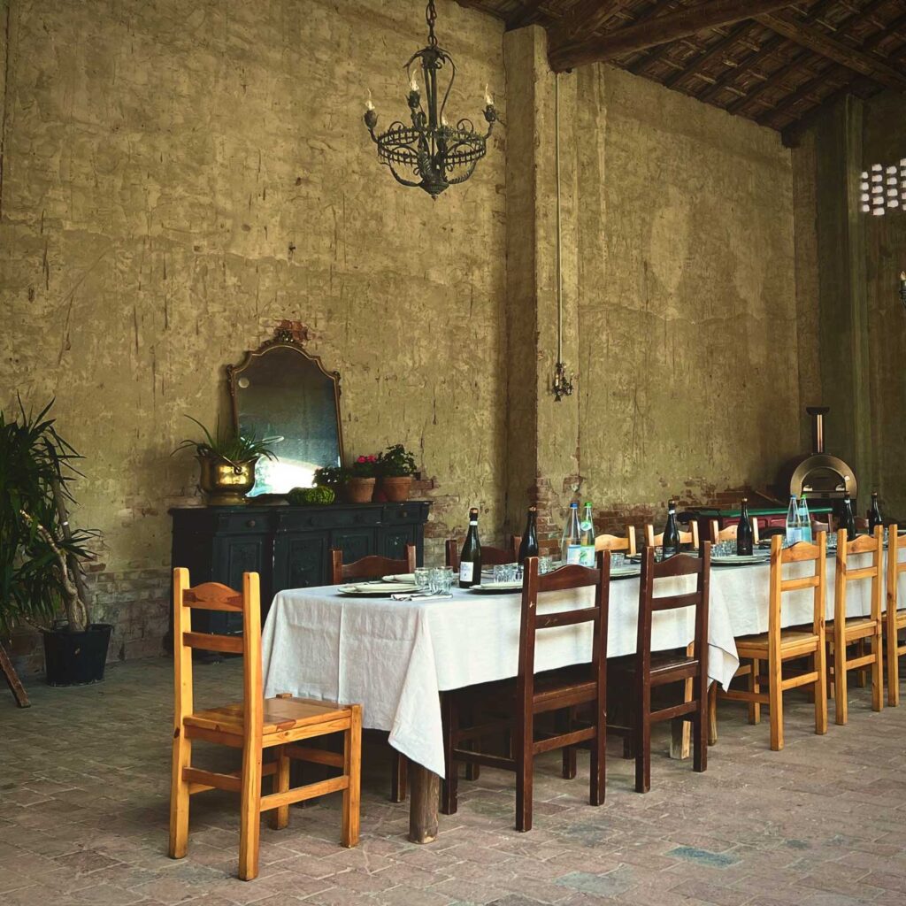 Rustikaler italienischer Speisesaal mit einem langen gedeckten Tisch, alten Holzmöbeln, Weinflaschen und einer charmanten, ländlichen Atmosphäre.