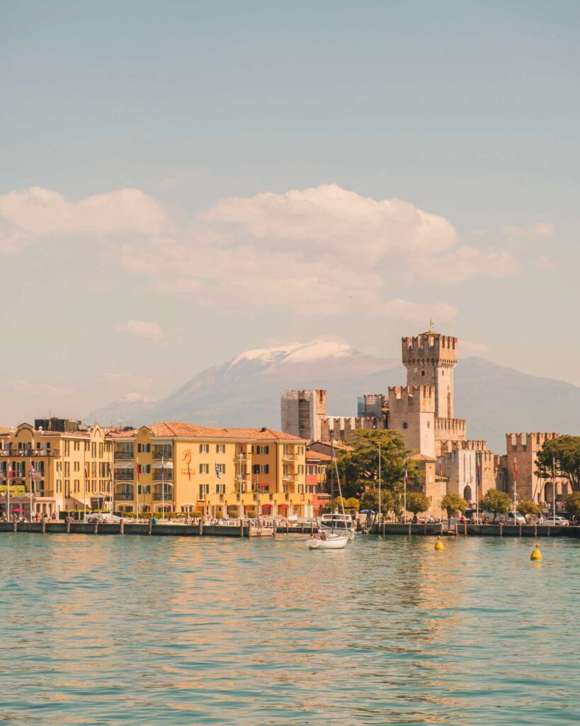 Das malerische Städtchen Sirmione am Gardasee mit der historischen Scaligerburg und den schneebedeckten Alpen im Hintergrund.