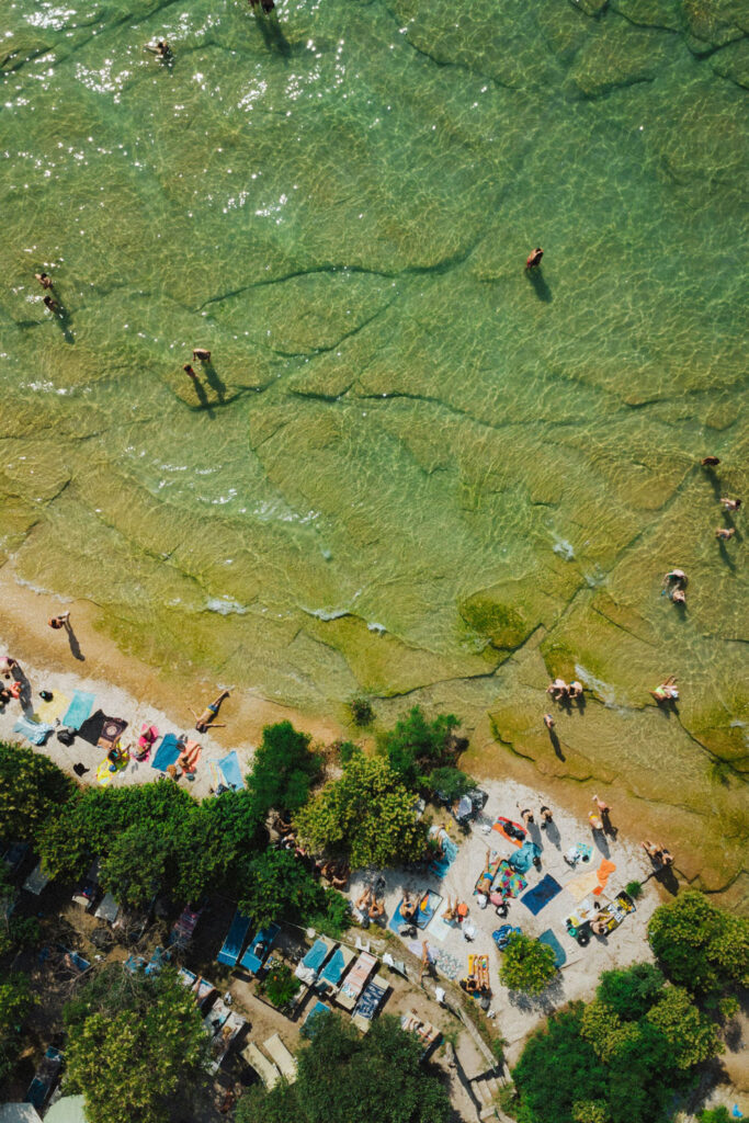 Luftaufnahme eines Strandes am Gardasee mit Menschen im klaren Wasser – perfekter Sommermoment für einen frischen Lugana.