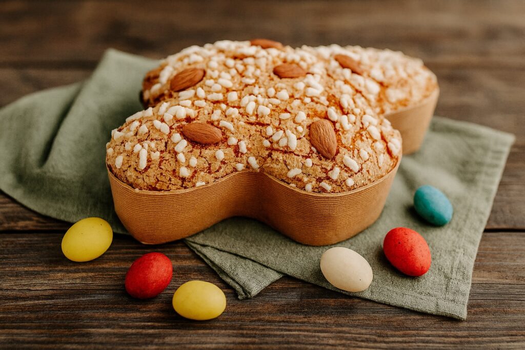 Traditionelle Colomba Pasquale mit knuspriger Mandel-Zuckerglasur auf einem grünen Tuch, umgeben von bunten Ostereiern – italienischer Osterklassiker in Taubenform.