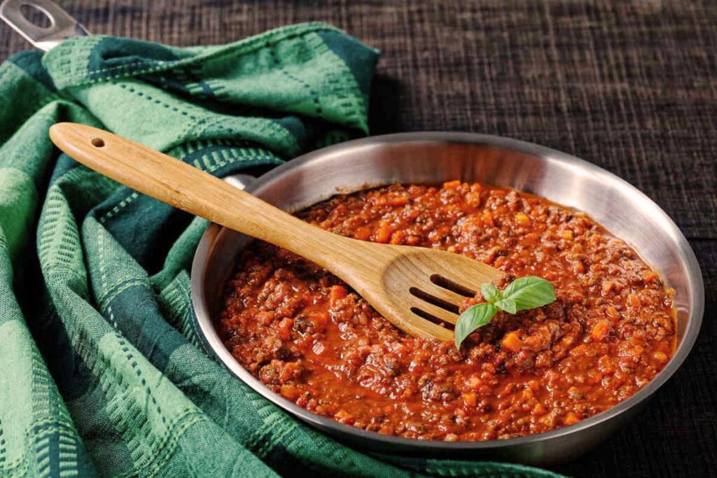 Eine Pfanne mit hausgemachter Bolognese-Sauce, garniert mit einem frischen Basilikumblatt, auf einem grünen Küchentuch.