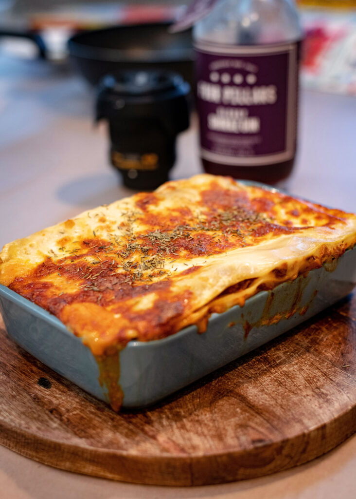 Frisch gebackene Lasagne al Forno in einer blauen Auflaufform mit knuspriger Kruste, serviert auf einem runden Holzbrett.