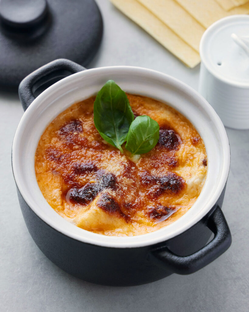 Einzelportion Lasagne al Forno in einer kleinen schwarzen Ofenform mit goldbrauner Kruste und frischem Basilikum.