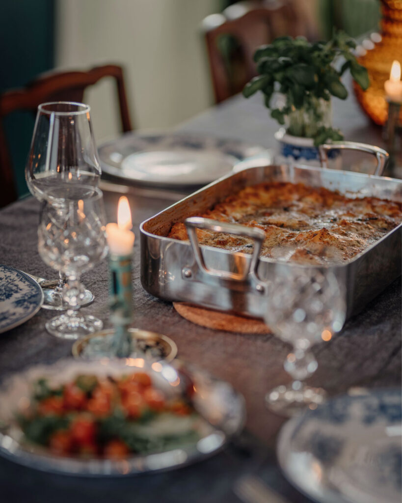 Frisch gebackene Lasagne in einer Edelstahlform auf gedecktem Tisch mit Kerzenschein – authentisches italienisches Abendessen in familiärer Atmosphäre.