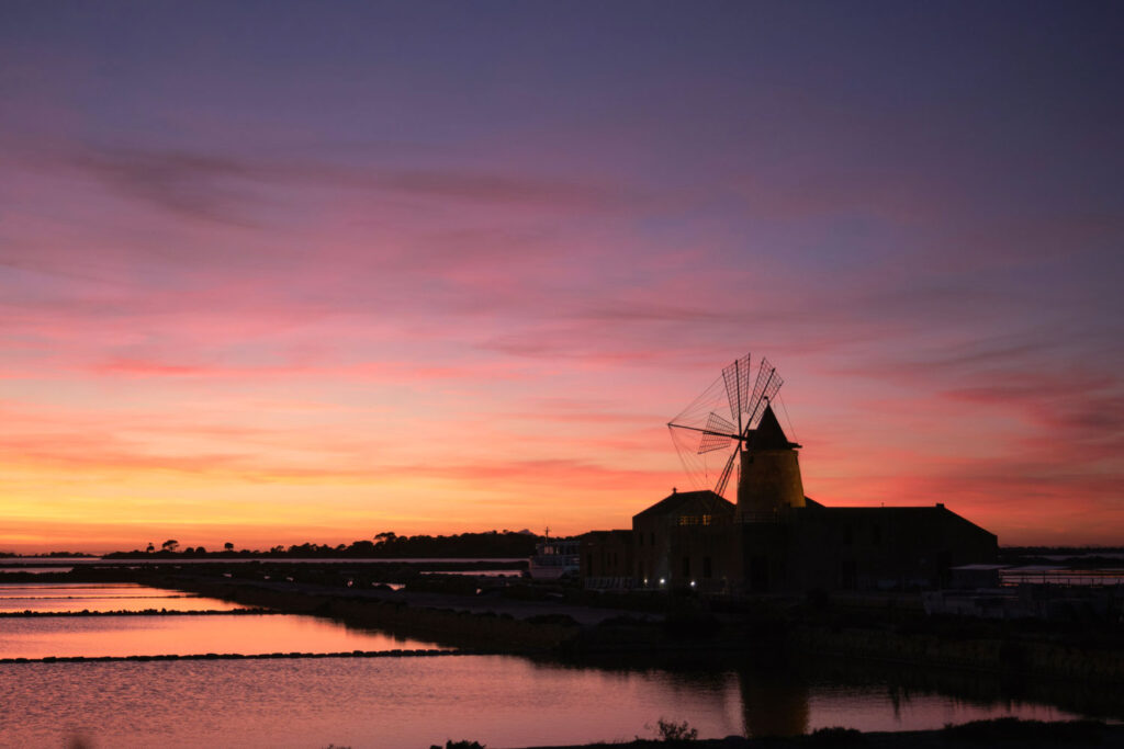 Stimmungsvolle Abenddämmerung über den Salinen von Marsala mit Windmühle – Symbol für die historische Weinregion.