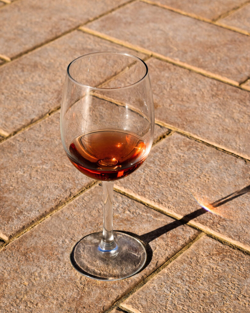 Ein Glas Marsalawein auf warmen Terrakottafliesen – goldbraune Reflexe im Sonnenlicht.