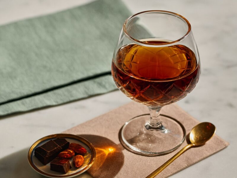 Ein edles Glas Marsalawein auf Marmortisch mit dunkler Schokolade, Mandeln und goldenem Löffel – stilvolle Komposition zur Likörweinverkostung.