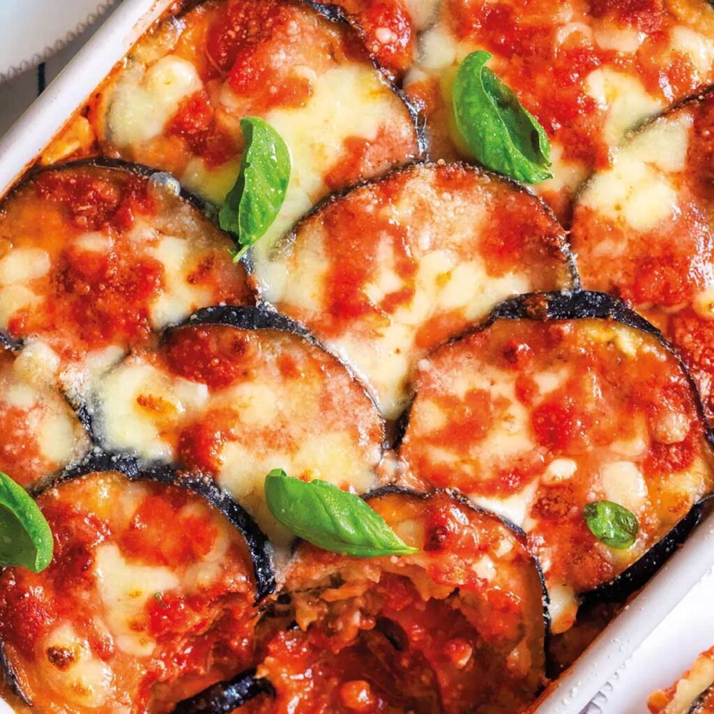 Nahaufnahme einer knusprigen Parmigiana di Melanzane mit geschmolzenem Mozzarella und goldbraun überbackenem Käse, garniert mit frischem Basilikum