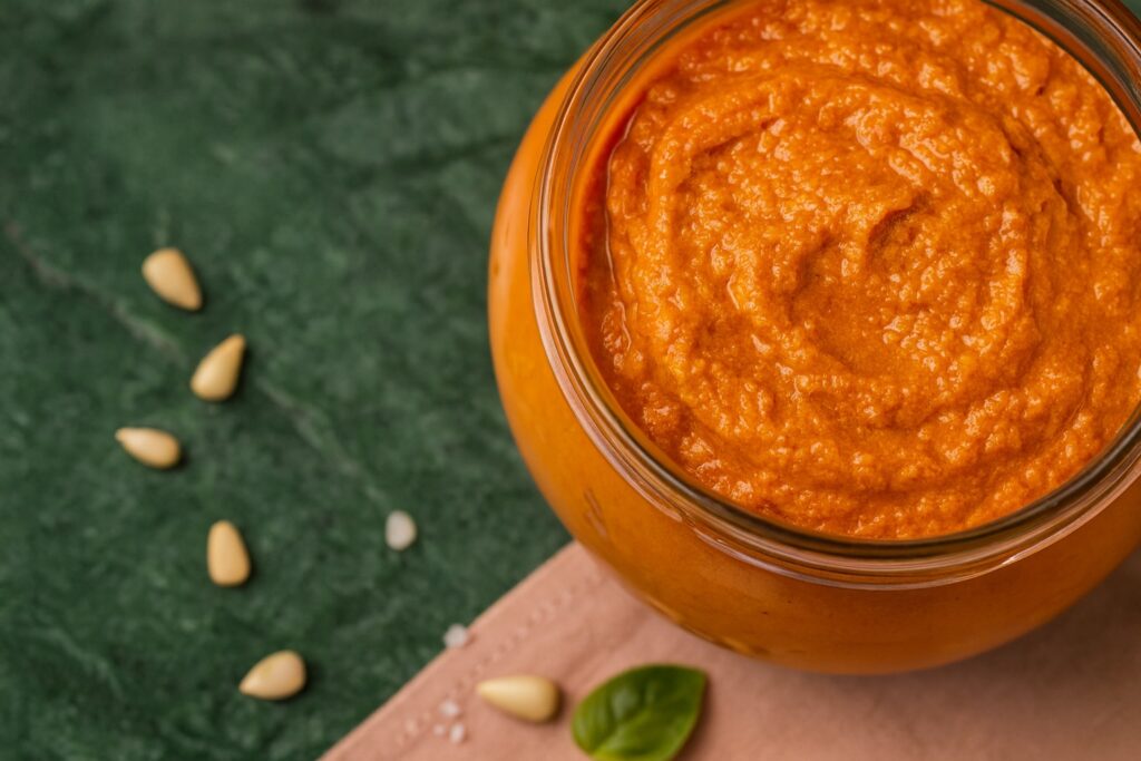 Nahaufnahme eines Glases mit sizilianischem Pesto – leuchtend orange Farbe mit Mandeln und Basilikum