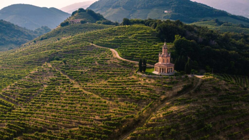 Die idyllische Landschaft der Prosecco-Hügel mit einer imposanten Kirche im Zentrum. Die weiten, terrassenförmigen Weinberge erstrecken sich über sanfte Hänge.