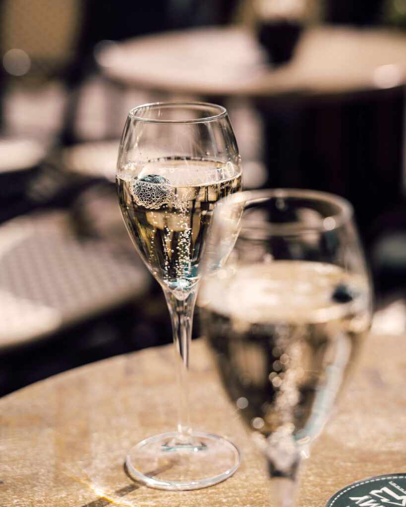 Zwei Gläser Prosecco auf einem Café-Tisch im Freien, mit feinen Perlen und sommerlicher Lichtstimmung – italienischer Lebensstil in der Sonne.