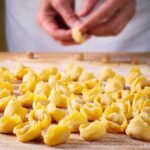 Viele frisch geformte Tortellini liegen auf einer bemehlten Holzfläche, bereit für die Weiterverarbeitung