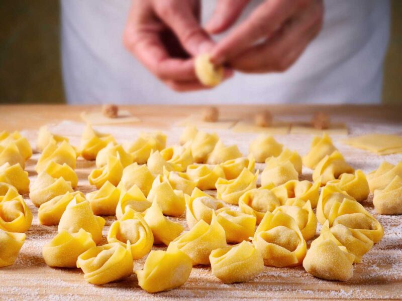 Viele frisch geformte Tortellini liegen auf einer bemehlten Holzfläche, bereit für die Weiterverarbeitung