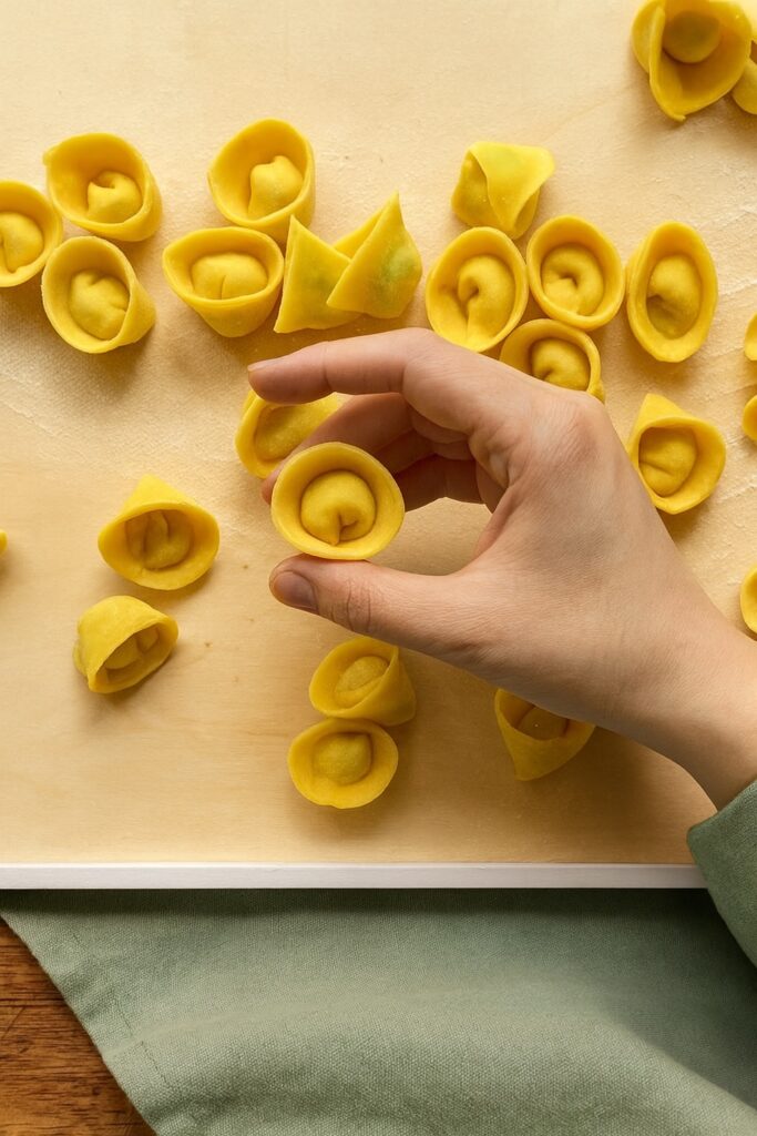 Nahaufnahme einer Hand, die einen frisch geformten Tortellino hält – goldgelbe Pasta mit sorgfältig gefalteter Form.