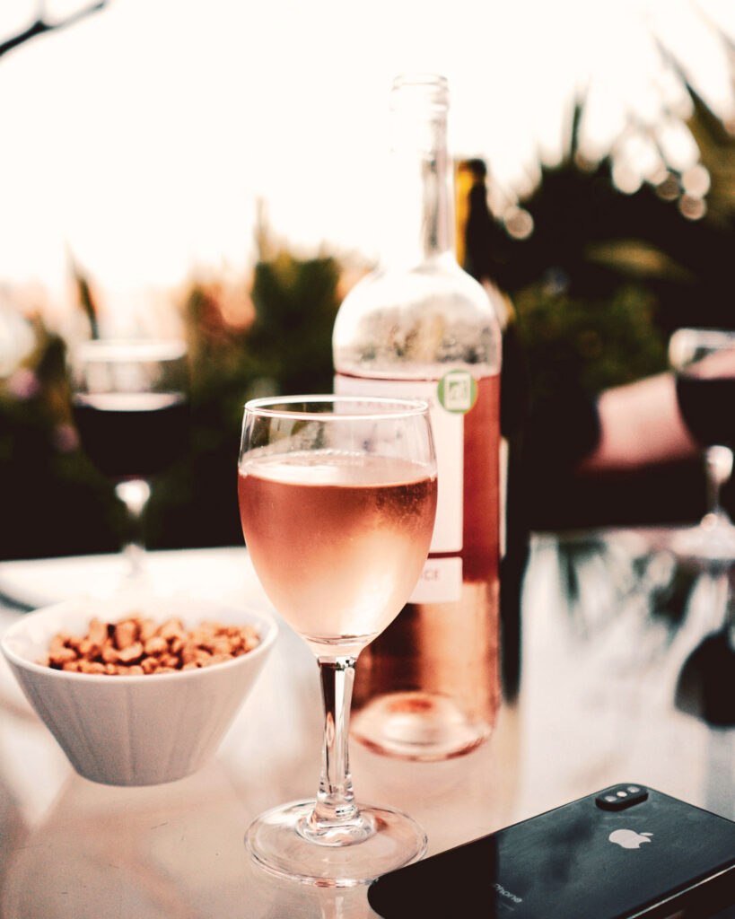 Ein Glas Bardolino Chiaretto Roséwein auf einem Glastisch mit Nüssen in einer Schale und einem Smartphone im Vordergrund – sommerliche Aperitivo-Stimmung bei Sonnenuntergang.
