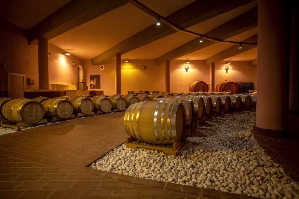 Stimmungsvolle Weinkellerei mit aufgereihten Eichenfässern auf Kieselsteinen in gedämpfter Beleuchtung.