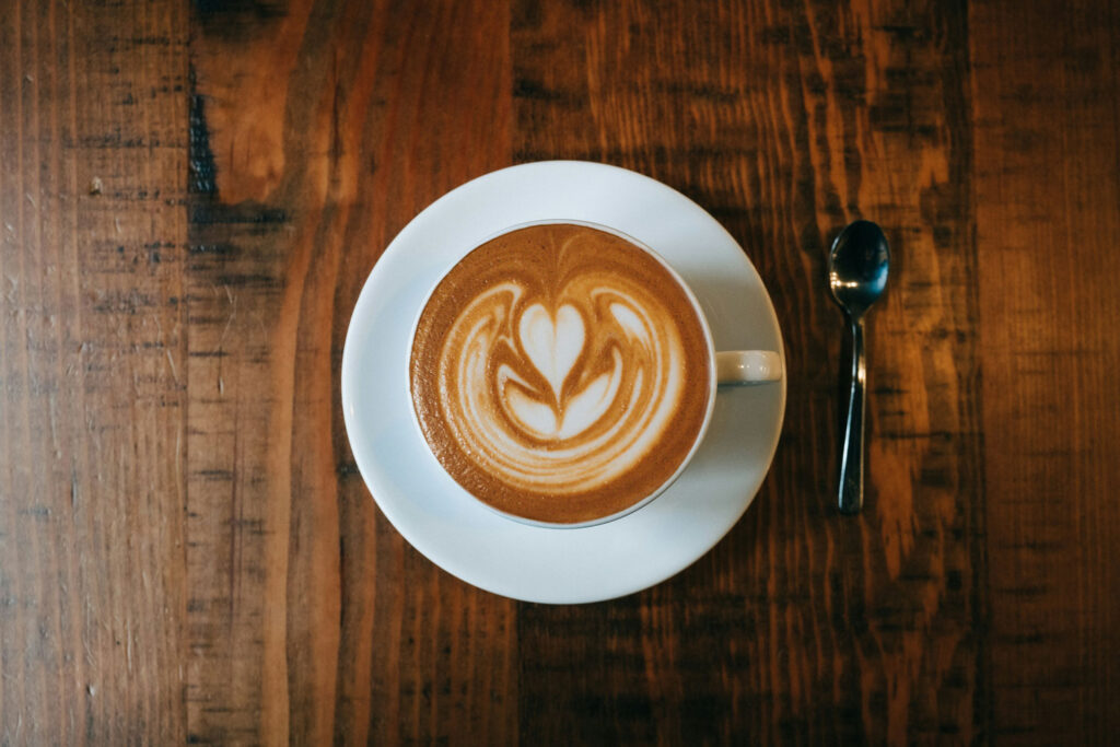 Cappuccino von oben fotografiert, mit wunderschöner Latte Art in Herzform auf dem Milchschaum, serviert auf einem Holztisch.