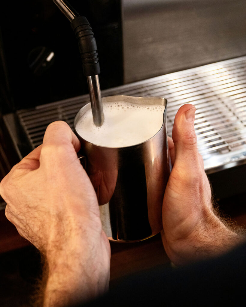 Frisch aufgeschäumte Milch wird in einer silbernen Kanne mit einer Dampfdüse einer Espressomaschine zubereitet.