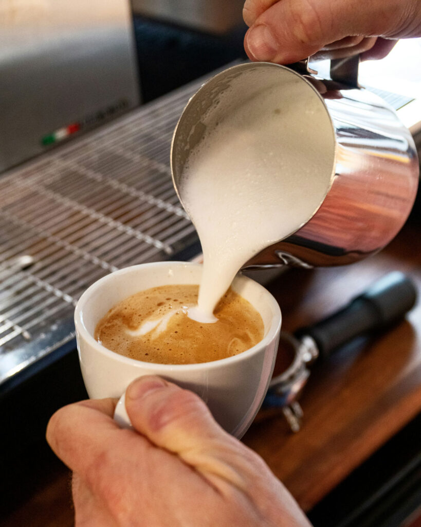 Barista gießt den fein aufgeschäumten Milchschaum in eine Cappuccino-Tasse, um das perfekte Verhältnis zu erreichen.
