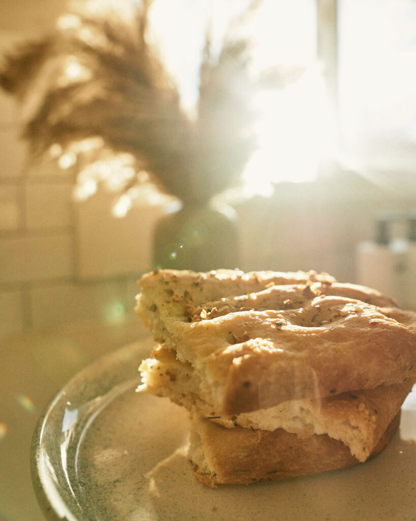 Zwei Stücke luftige Focaccia auf einem Keramikteller, im Sonnenlicht fotografiert.