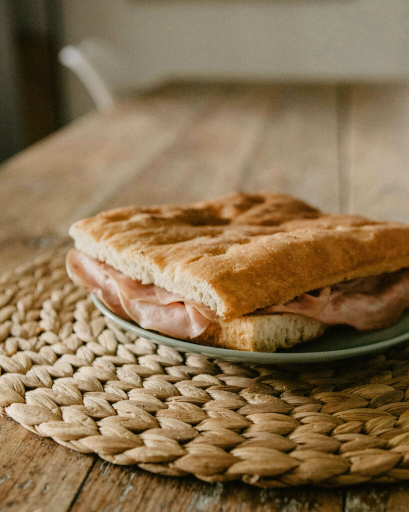 Focaccia-Sandwich mit Mortadella auf einem rustikalen Holztisch serviert.