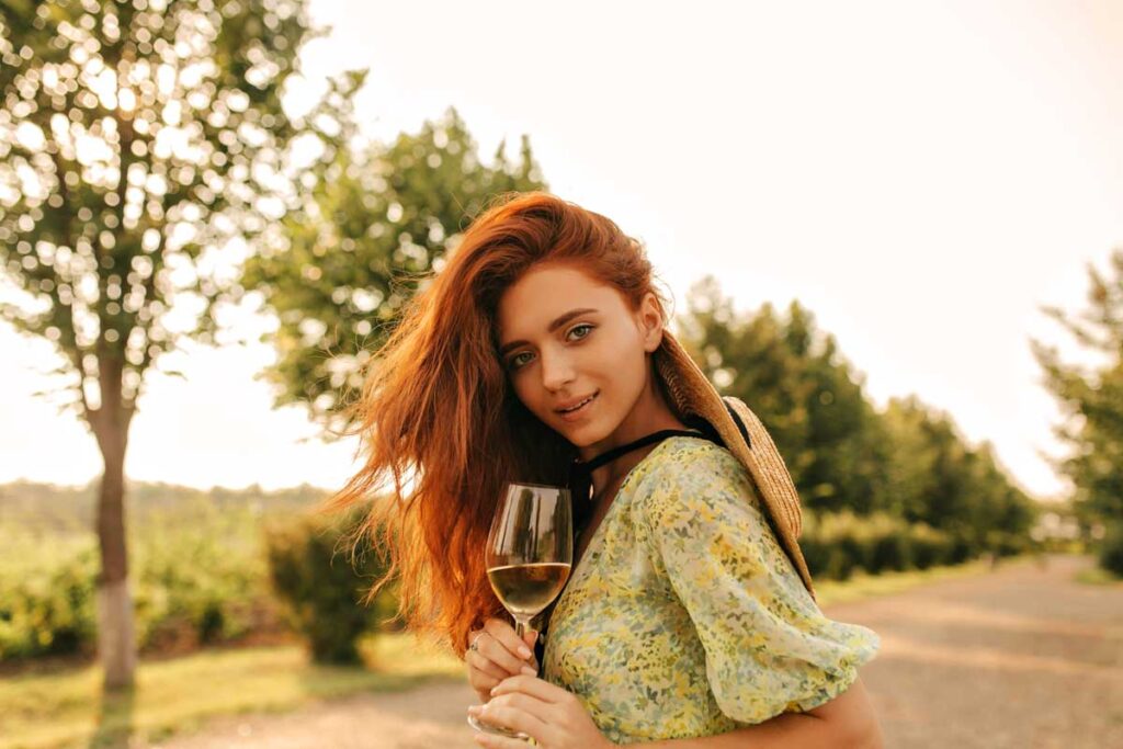 Junge Frau mit einem Glas Gavi Weißwein in der Hand, genießt den Ausblick auf die Weinberge an einem sonnigen Nachmittag.
