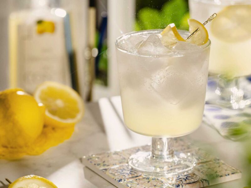 Erfrischender Limoncello Spritz im Glas auf einem mediterranen Untersetzer, dekoriert mit frischen Zitronenscheiben und Eiswürfeln.