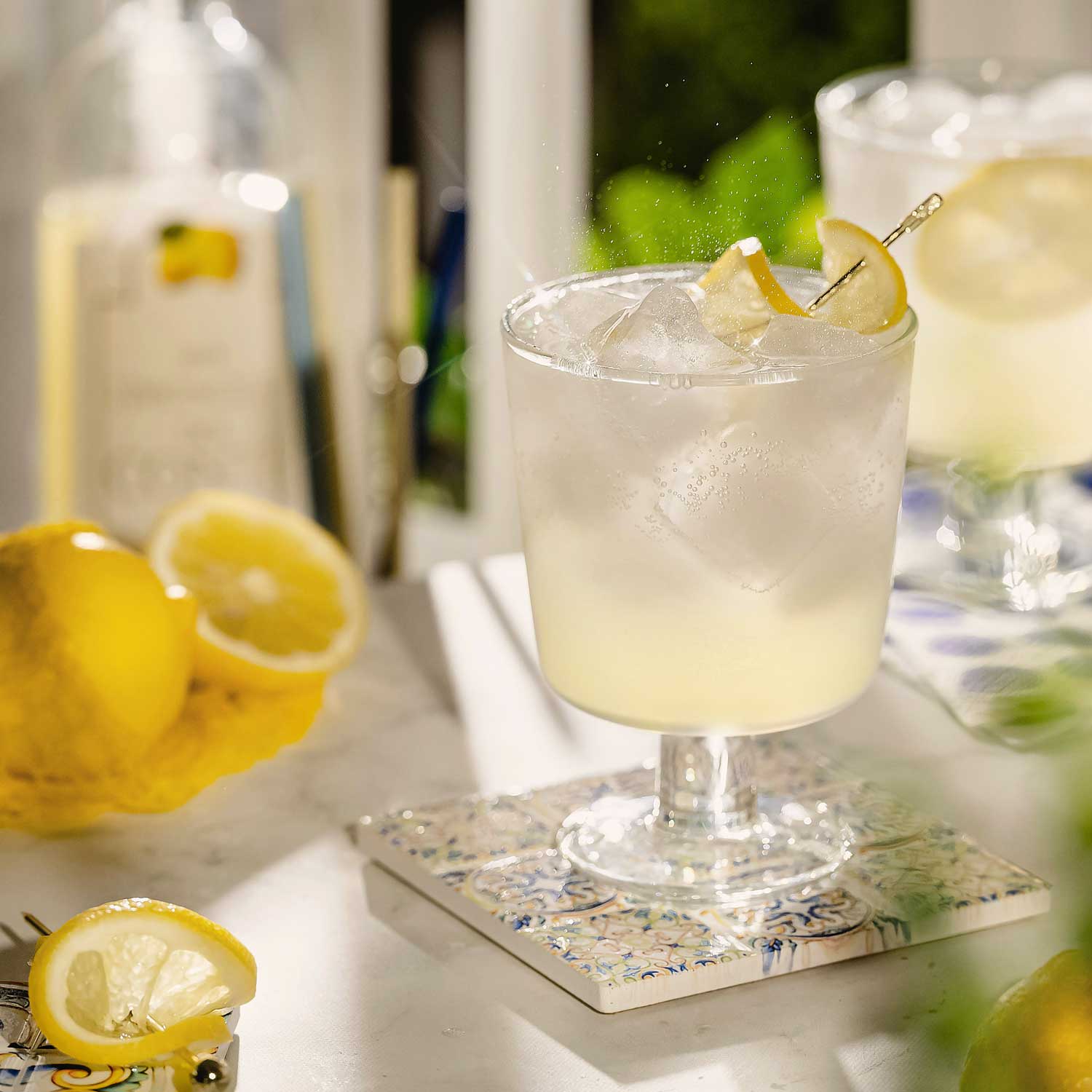 Erfrischender Limoncello Spritz im Glas auf einem mediterranen Untersetzer, dekoriert mit frischen Zitronenscheiben und Eiswürfeln.